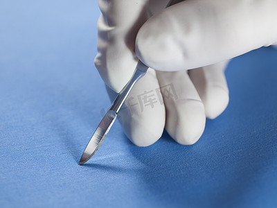 外科医生在一只手套，拿起手术刀的手.