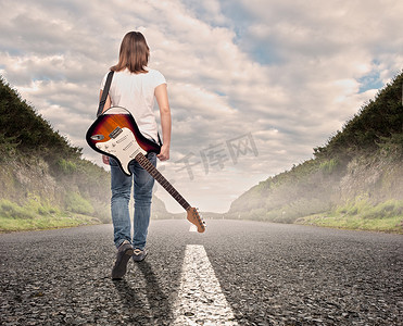 行走在路上摄影照片_年轻的音乐家女人走在路上