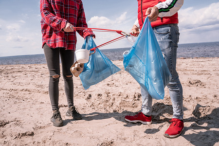 带着垃圾袋的夫妇和在沙滩上捡垃圾的拾荒者的剪影 