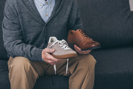 裁剪的老人拿着经典和现代的鞋在手的看法 