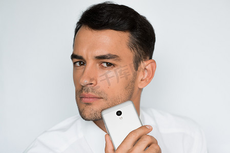 英俊男人的肖像发送手机上的文本与灰色背景隔离。技术和连接理念。年轻的白种商人在演播室用智能手机摆姿势.