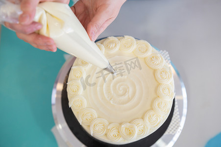 厨师女厨师摄影照片_女糕点厨师在面包店装饰奶油和奶酪蛋糕。用奶油糕点袋装饰蛋糕。头版头条。庆祝食物概念