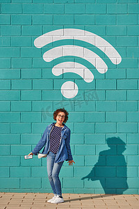 在阳光灿烂的一天，一个快乐的女人站在明亮的蓝色墙壁上，头顶上方挂着无线电通信信号。高质量的照片.