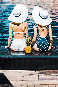 在游泳池里, 穿着泳衣和帽子坐着菠萝的女孩的背视图