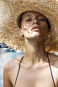 stylish摄影照片_Woman in hat and black stylish swimsuit poses near swimming pool enjoying sun. Phuket island, Thailand. High fashion look.