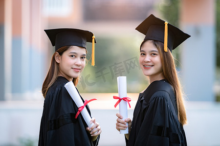 毕业照片摄影照片_年轻快乐的亚洲女大学毕业生身着毕业礼服，身临其境，在大学校园里获得了学位证书，以庆祝她们的教育成就。教育库存照片