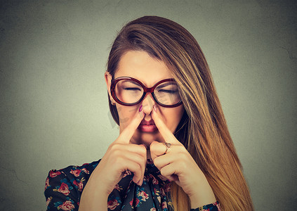 woman pinches nose with fingers looks with disgust bad smell