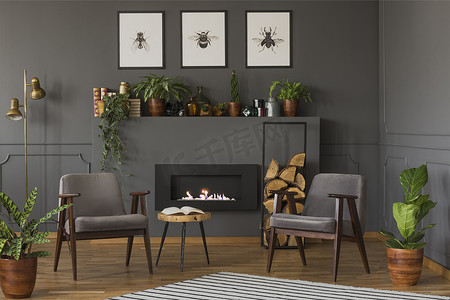 平面海报摄影照片_木桌之间的灰色扶手椅在复古平面内部与壁炉下的海报。真实照片