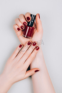 漂亮的深红色美发与一瓶指甲油在灰色背景的手。程序概念。平铺风格.