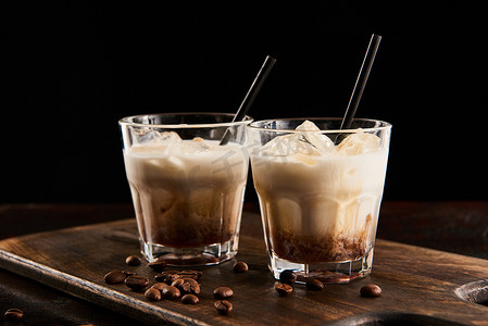 isolated摄影照片_white russian cocktail in glasses with straws on wooden board with coffee grains isolated on black