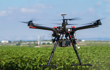 hexacopter摄影照片_无人驾驶飞机悬停在绿色的田野