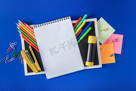 空白笔记本和蓝色背景的各种信纸的空黑板的顶部视图 
