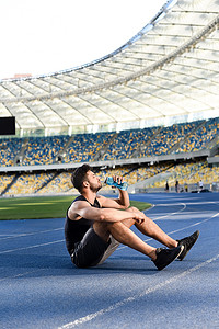 英俊潇洒的运动员在体育场跑道上休息喝水