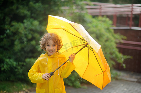 有一把黄色雨伞的开朗的男孩在院子里下着雨.