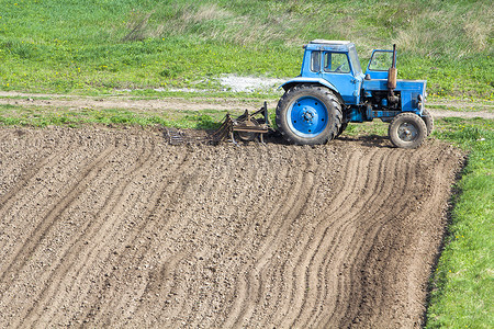 蓝色尘土飞扬的拖拉机与苗床耕种站在新犁和耕地的边缘, 准备播种的土壤。农业、农业和农业机械概念.