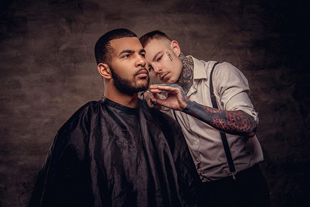 老式的专业纹身理发师用剪刀和梳子给非洲裔美国人的客户理发。在深色纹理背景下隔离.