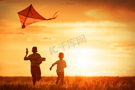 风筝风筝摄影照片_日落时孩子们在田野里放风筝