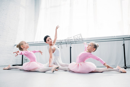 可爱芭蕾摄影照片_年轻芭蕾舞老师训练可爱的小芭蕾舞在芭蕾演播室