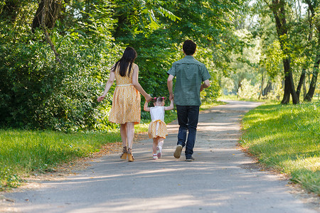回顾快乐的家庭手牵手走在小径上，在美丽的绿色公园里度过时光的情景.