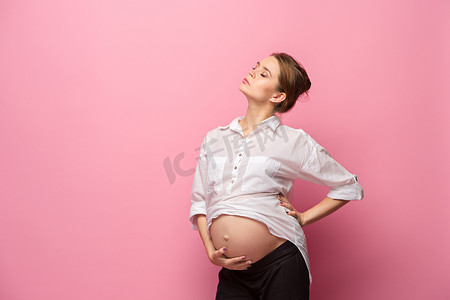 年轻美丽的孕妇站在粉红的背景上