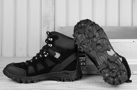冬季防滑安全摄影照片_特写一双黑色工作靴，用于冬季安全，脚尖为钢制，鞋底为灰色木制底座和金属工具箱的防滑材料底。舒适屈曲安全工作人员的概念，屋顶.