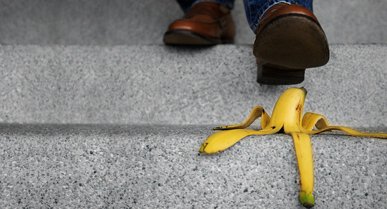 踩摄影照片_日常生活中的意外概念。男人踩着香蕉皮踩下楼梯。保险或商业隐喻