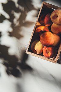 浅色大理石摄影照片_在浅色大理石表面上满是新鲜桃子的木箱的顶部视图