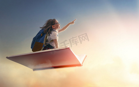 逆风飞翔摄影照片_回学校去！快乐可爱的勤劳的孩子在夕阳的背景下在书上飞翔.教育和阅读的概念。想象力的发展.