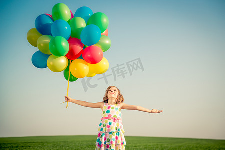 快乐的孩子在户外玩色彩艳丽的气球.在蓝天背景下,孩子们在绿色的春田里玩得很开心.健康和积极的生活方式概念