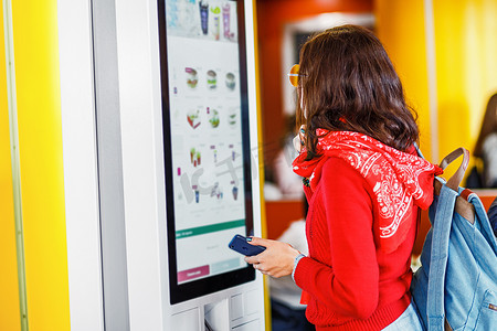 订购弹窗摄影照片_时髦的亚洲妇女在快餐餐厅的电子菜单上, 在触摸屏自助服务机上订购食物