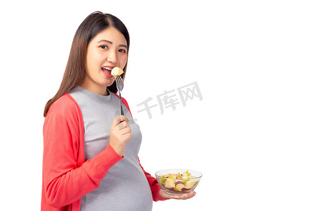怀孕的年轻亚洲女人吃新鲜的水果沙拉，水果沙拉是婴儿或胎儿的健康食品。怀孕的母亲拿着一袋水果沙拉.怀孕、产前、母性、保健概念