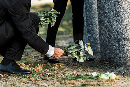 高龄男子在墓碑和女人附近献花的裁剪视图 