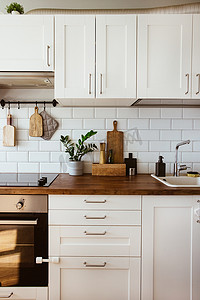 瓷砖摄影照片_厨房黄铜器皿，厨师配件。用白色瓷砖墙和木桌挂厨房。厨房背景上的绿色植物