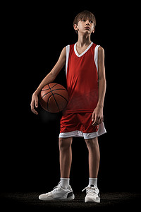 全长的少男肖像，身穿红色制服的篮球运动员，在黑色背景下摆出孤立的球姿