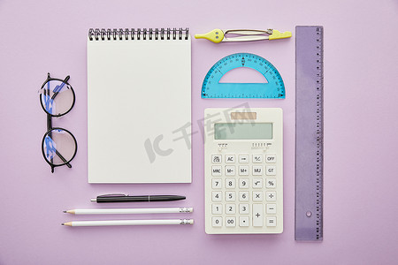 尺子与圆规摄影照片_笔记本电脑旁边的尺子和计算器的顶部视图和用紫色隔开的文具 