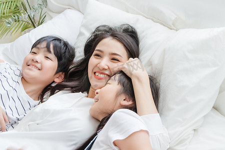 快乐的亚洲家庭在卧室的床上微笑着母亲、儿子和女儿。妈妈，儿子和女儿在家里玩得开心。母子之间的爱情关系或感情纽带。人的生活方式概念