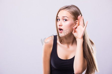 收礼物的女人摄影照片_收起来的女人握着她的手靠近耳朵和听小心地隔离墙灰背景上。人类情感的肢体语言面部表情