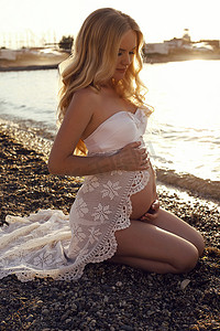 beautiful pregnant woman with long blond hair posing on sunset beach  