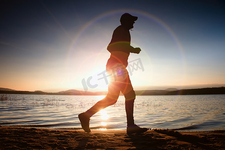 赛跑者在太阳光线在海滩上。运动员戴棒球帽，慢跑在以上海上日出