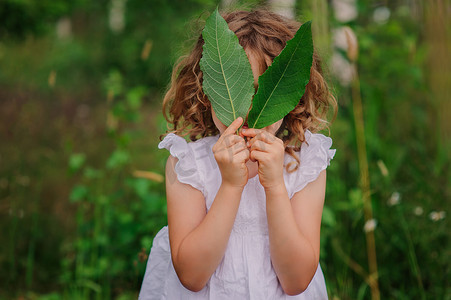 summer水纹摄影照片_child girl playing with leaves in summer forest with birch trees. Nature exploration with kids. Outdoor rural activities.