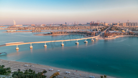 迪拜棕榈岛摄影照片_朱美拉棕榈岛间隔拍摄日落时在迪拜，阿拉伯联合酋长国。朱美拉棕榈是人工和独特的岛屿，在迪拜与如今的背景。别墅和单轨列车