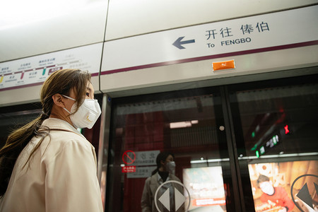 戴口罩的年轻女人站在地铁站台上