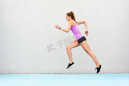 奔跑比赛摄影照片_她的体形很好，可以参加比赛了。一位年轻貌美的女运动员在跑道上奔跑的全景照片