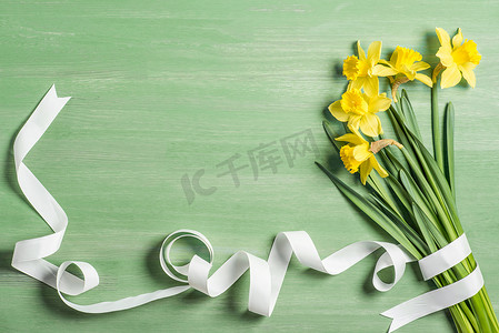 从上面的白色丝带包裹在绿色背景上的水仙花花束