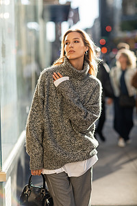 穿着灰色衣服的年轻时尚女人手握手提包，在阳光灿烂的纽约市大街上摆姿势 