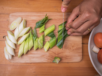 女手用菜刀在木板上切割日本长葱或日本葱或绿葱。女人正在厨房准备家里的食物。烹调概念.