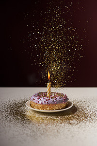 isolated摄影照片_burning candle in middle of doughnut with falling sparkles on white table isolated on black