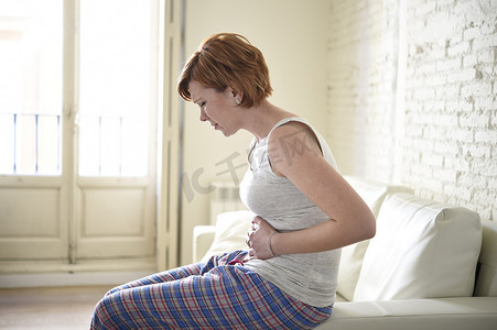 女孩在沙发沙发上抱着受伤的肚子遭受胃痉挛和期间疼痛