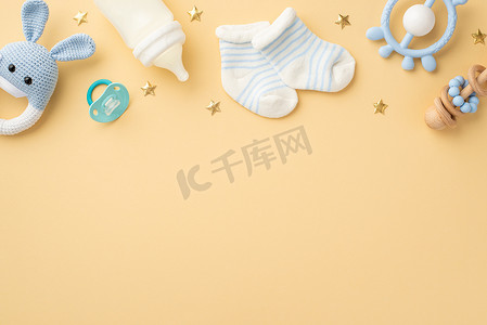 婴儿与奶瓶摄影照片_婴儿用品概念。针织兔子玩具蓝色聚醚奶瓶小袜子奶嘴和金色星辰在孤立的白色米色背景与空旷的空间的俯瞰照片
