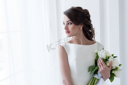 美丽的新娘举行婚礼花束和看窗口